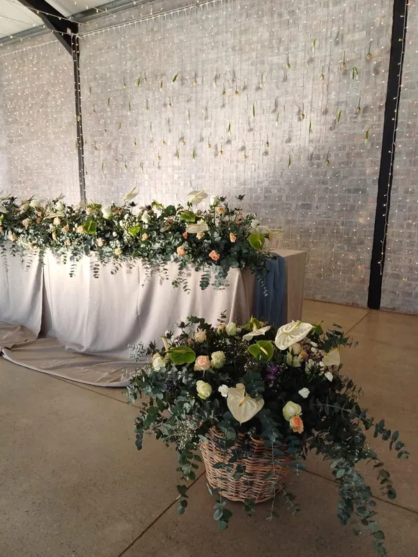 An anthurium and rose basket arrangement in front of string lights.