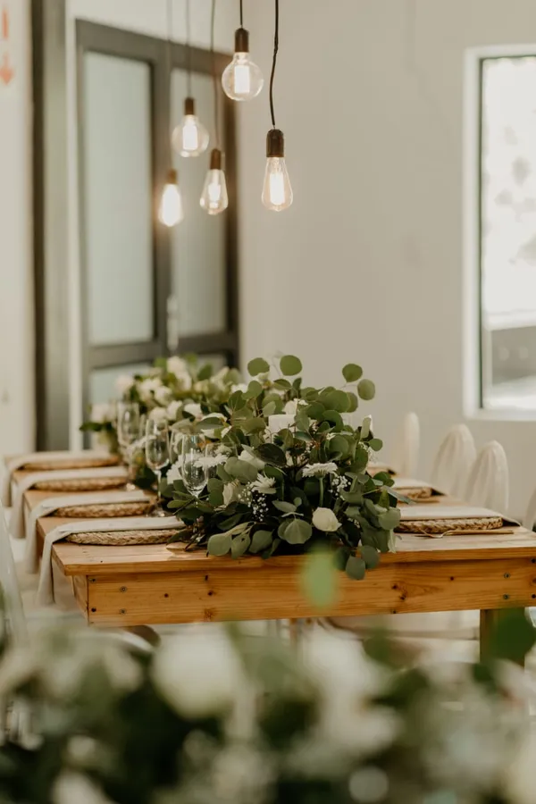 A reception table styled with hanging bulb lights and a greenery runner.