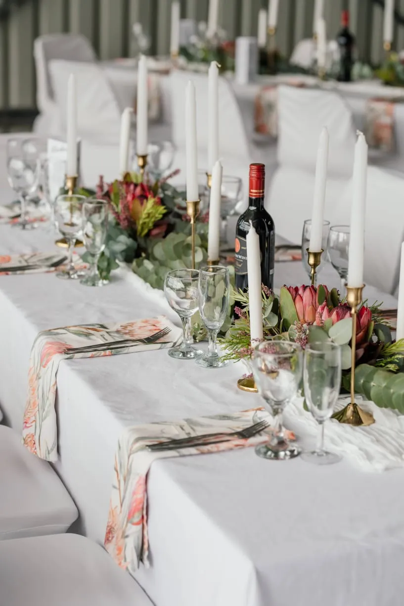 A candlelit table runner with proteas and a bottle of wine.
