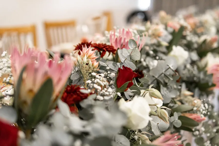 A rich protea, red rose, and eucalyptus centerpiece arrangement.
