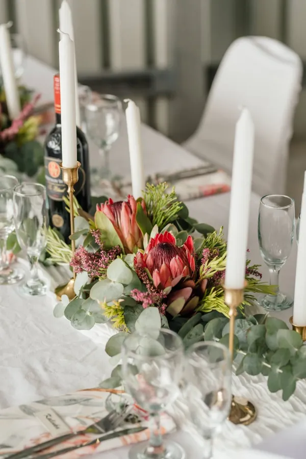 Red proteas displayed with gold candlesticks on a reception table.