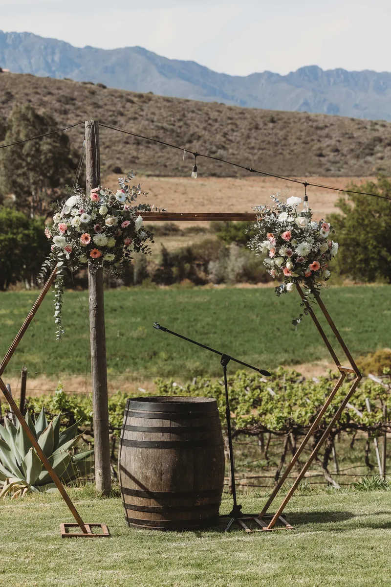 A wooden ceremony arch with floral clusters overlooking a vineyard and mountains.